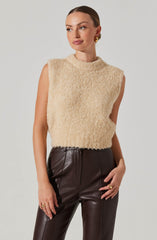 A woman is wearing a sleeveless, high-neck, cream-colored, fuzzy sweater paired with high-waisted, dark brown leather pants.
