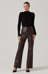 A woman is wearing a fitted black ribbed long-sleeve turtleneck sweater and high-waisted, wide-leg brown leather pants. She is also wearing black high-heeled shoes.