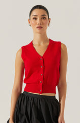 A woman is wearing a sleeveless red knit vest with a V-neckline and button-down front. The vest has a fitted ribbed hem at the waist, creating a cropped look. She is paired with black, loose, gathered pants.
