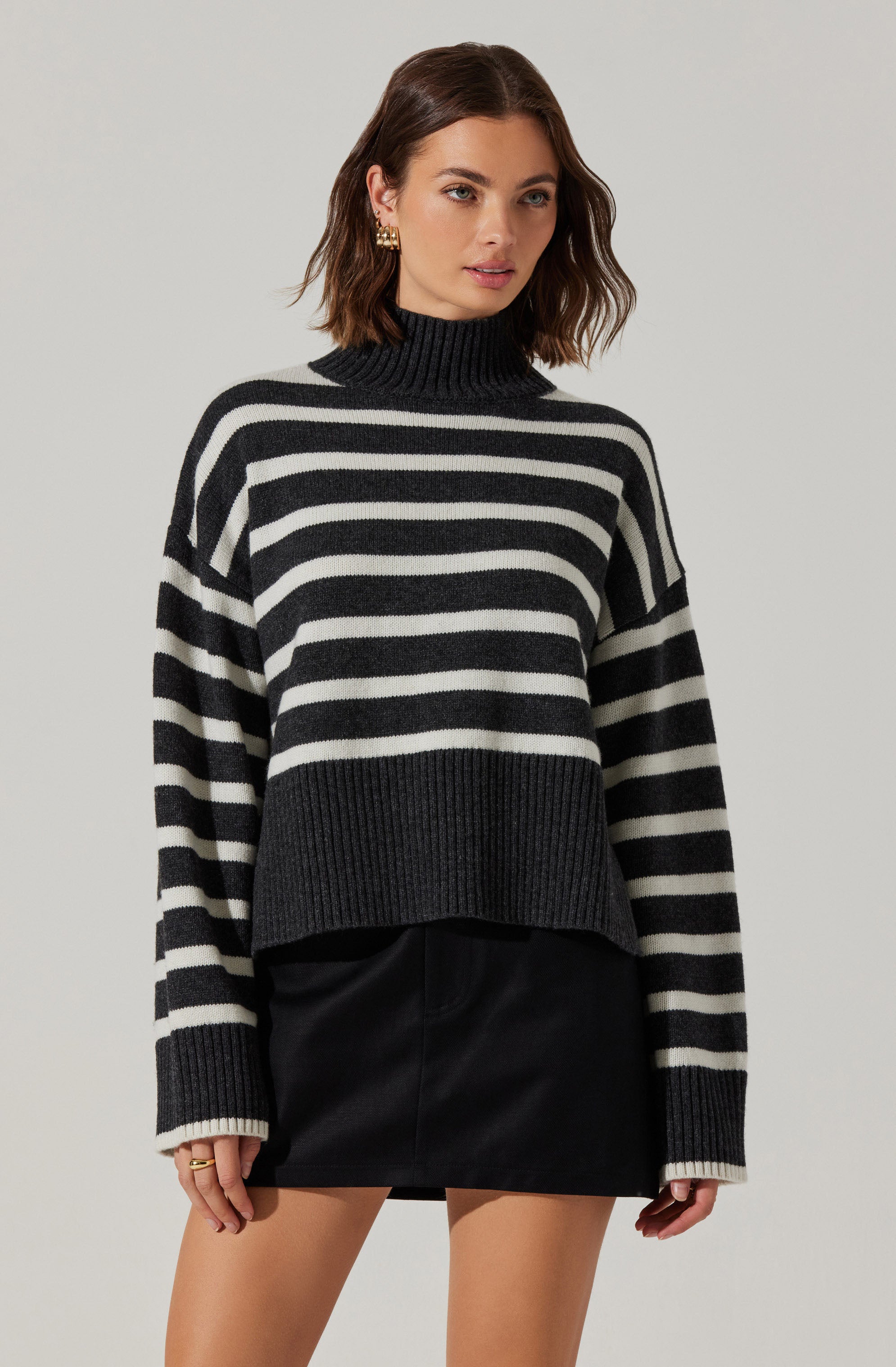 A woman is wearing a black and white horizontally striped turtleneck sweater with a loose fit and ribbed cuffs and hem, paired with a black leather mini skirt.