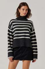 A woman is wearing a black and white horizontally striped turtleneck sweater with a loose fit and ribbed cuffs and hem, paired with a black leather mini skirt.