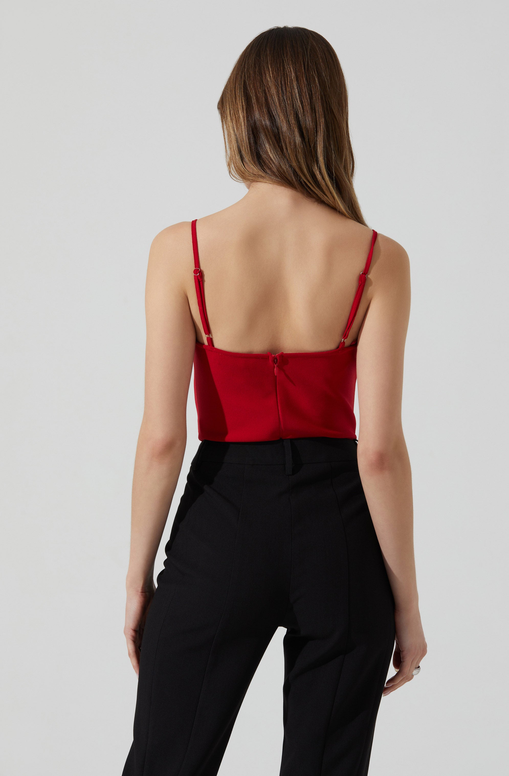 A woman is wearing a fitted red spaghetti strap top with a back zipper, paired with high-waisted black trousers.