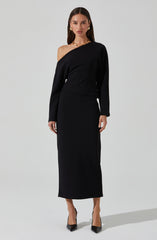 A woman is wearing an elegant, all-black outfit consisting of a long skirt and a matching off-the-shoulder top. The top features a relaxed fit with one shoulder exposed, while the skirt is high-waisted and flows down to her ankles. She accessorizes with gold hoop earrings, layered necklaces, and rings, completing her sophisticated look with black pointed-toe high heels.