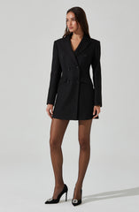 A woman is wearing a tailored black double-breasted blazer-style coat with wide lapels and long sleeves. The coat features decorative buttons and appears to be fitted at the waist, ending just above the knees. She is also wearing sheer black high heels with pointed toes and decorative embellishments on the front.