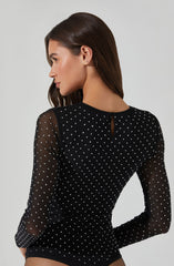 A woman is wearing a black long-sleeve top made of sheer fabric with small white polka dots. The top has a small keyhole opening at the back near the neckline.