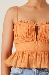 A woman is wearing an orange sleeveless top with thin spaghetti straps. The top features a textured, crinkled fabric with a ruffled, peplum-style hem. The bodice has a small keyhole opening at the front.