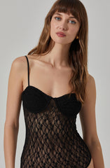 A woman is wearing a black, lace, semi-sheer lingerie top with thin spaghetti straps. The top features a fitted bust with lace cups and a patterned lace body.