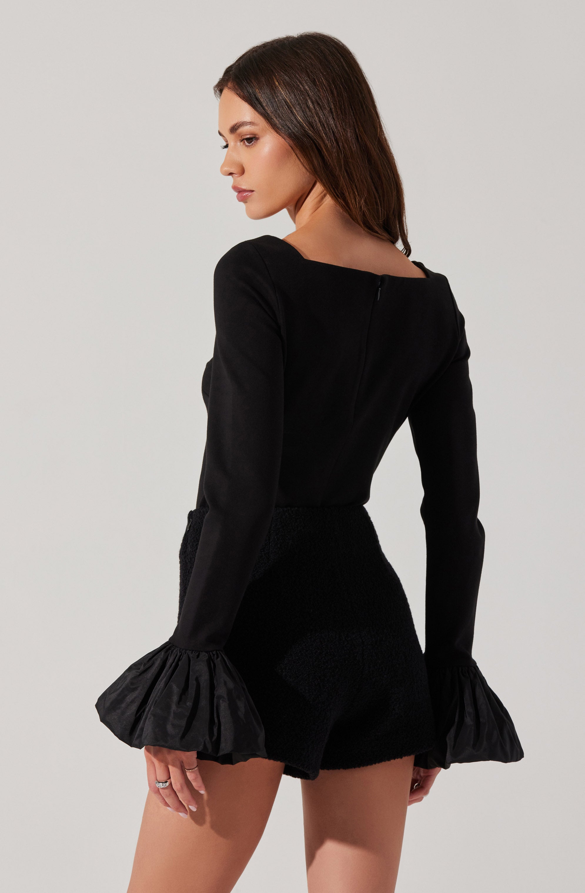 A woman is wearing a black long-sleeve top with dramatic ruffled cuffs and matching black shorts.