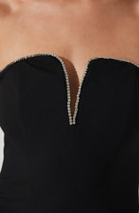 A close-up of a black strapless dress with a sweetheart neckline, edged with sparkling rhinestones along the top and down the center.