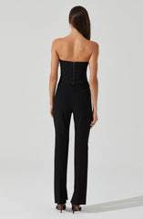 A woman is wearing a strapless black top with a zipper at the back, paired with black, straight-leg trousers. She is also wearing black high-heeled shoes.