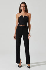 A woman is wearing a strapless black top with a front zipper detail and matching black high-waisted trousers with a slight flare and small front slit at the hem.