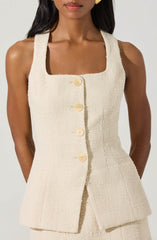A woman wearing a sleeveless, cream-colored, textured fabric dress with a square neckline. The dress features a button-down front with large, round, cream-colored buttons and a fitted silhouette.
