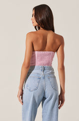A woman is wearing a pink, strapless, gathered textured top and high-waisted, light-wash denim jeans. The top is fitted and ruched, and the jeans have a classic, relaxed fit with visible back pockets.