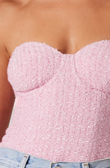 A close-up of a woman wearing a strapless pink textured top embellished with small, shiny beads and sequins. She is also wearing light-wash denim jeans.