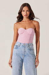 A woman is wearing a strapless pink textured top with a sweetheart neckline. She pairs it with high-waisted, light-wash denim jeans featuring a classic five-pocket design.