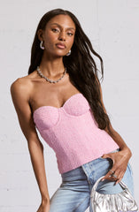 A woman is wearing a strapless pink textured top with structured cups. She has paired it with light blue high-waisted jeans. Her accessories include large hoop earrings, a chunky chain necklace, and a ring on her right hand. She is holding a shiny silver bag in her left hand.