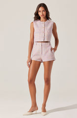A woman is wearing a sleeveless, pastel-colored, textured knit crop top with a round neckline and button closure at the front. She pairs it with matching high-waisted shorts that have a similar textured knit fabric and a notched hem. She completes the outfit with pointed-toe, cream-colored high heels.