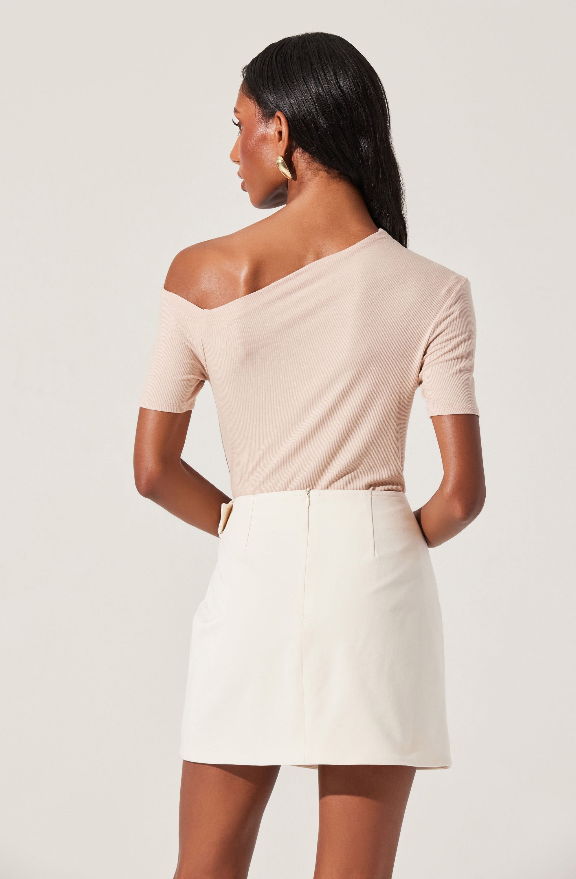 A woman is wearing a beige, off-the-shoulder top with short sleeves, paired with a high-waisted white skirt that reaches mid-thigh.