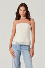 A woman is wearing a strapless, off-white, textured top with a frayed hem, paired with light-wash jeans.