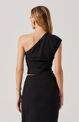 A woman is wearing a black, one-shoulder top with a draped, asymmetrical design. The top is fitted around her waist and has a slightly ruched appearance. She pairs it with a high-waisted black skirt that extends below the waist. The overall outfit is elegant and monochromatic.