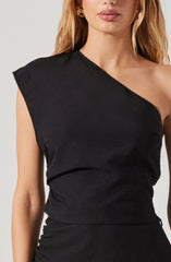 A woman is wearing a black sleeveless top with a one-shoulder design. The top has a smooth, slightly shiny fabric and fits snugly around her torso. She pairs it with gold hoop earrings.