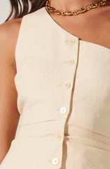 A close-up of a person's upper torso features a sleeveless, cream-colored dress with a slight textured weave. The dress has a round neckline and a row of small, round, matching cream-colored buttons running down the front. The fabric appears structured and tailored. The person is also wearing a chunky gold chain necklace that sits at the base of the neck.