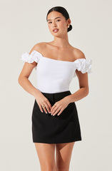 A woman is wearing an off-the-shoulder white top with ruffled sleeves and a fitted black skirt.