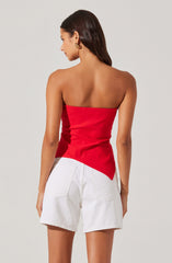 A woman wearing a strapless, fitted red top that is asymmetrical at the hem, paired with high-waisted white shorts that have large back pockets.