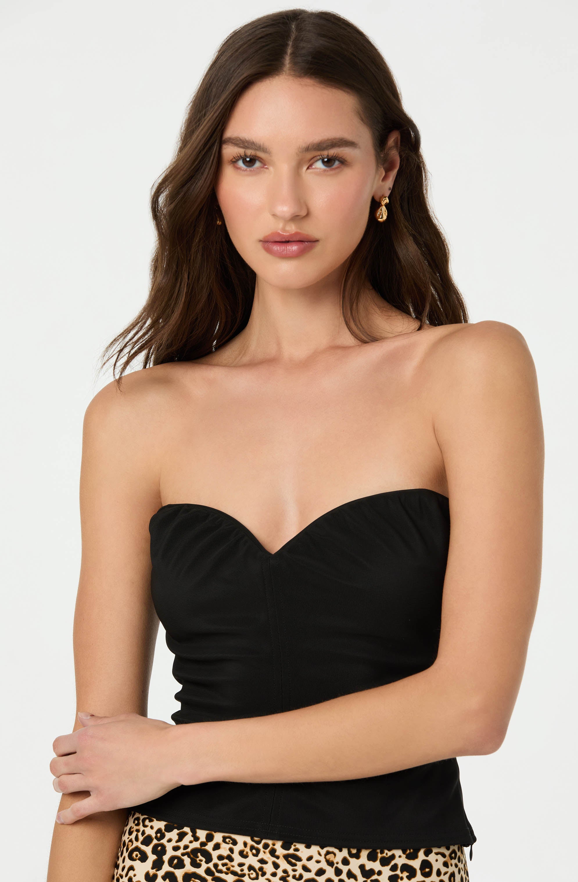 The woman is wearing a strapless black top with a sweetheart neckline and ruched details. She is also wearing gold drop earrings with round, intricate designs.