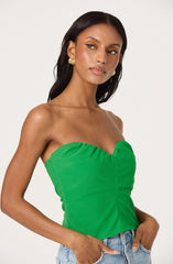 A woman is wearing a strapless, bright green top with a gathered detail along the bust and vertical seam down the front. She is also wearing light blue denim jeans and gold hoop earrings.