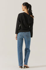 A woman is wearing a black long-sleeve top with a draped design on one shoulder and fitted at the waist. She is pairing it with high-waisted, straight-leg blue jeans and black open-toe high-heeled sandals. Her hair is styled in a sleek ponytail.