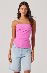 A woman is wearing a sleeveless pink halter top with a square neckline and ruched detailing at the sides. She pairs it with light-wash denim shorts.