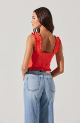 A woman is wearing a sleeveless red top with ruffled straps and ruffle detailing at the hem. She is also wearing high-waisted, light-wash jeans with prominent back pockets.