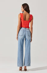 A woman is wearing a sleeveless red top with ruffled straps and a ruffled hem, paired with high-waisted, light-wash wide-leg jeans, and beige high-heeled shoes.