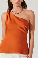 A woman wearing an orange satin one-shoulder top with a draped neckline. She accessorizes with gold hoop earrings and a gold and black beaded necklace.