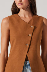 A woman is wearing a sleeveless, tan-colored vest with a V-neckline. The vest features a row of four light-colored buttons running diagonally down the front. The fabric appears to be a structured, woven material.