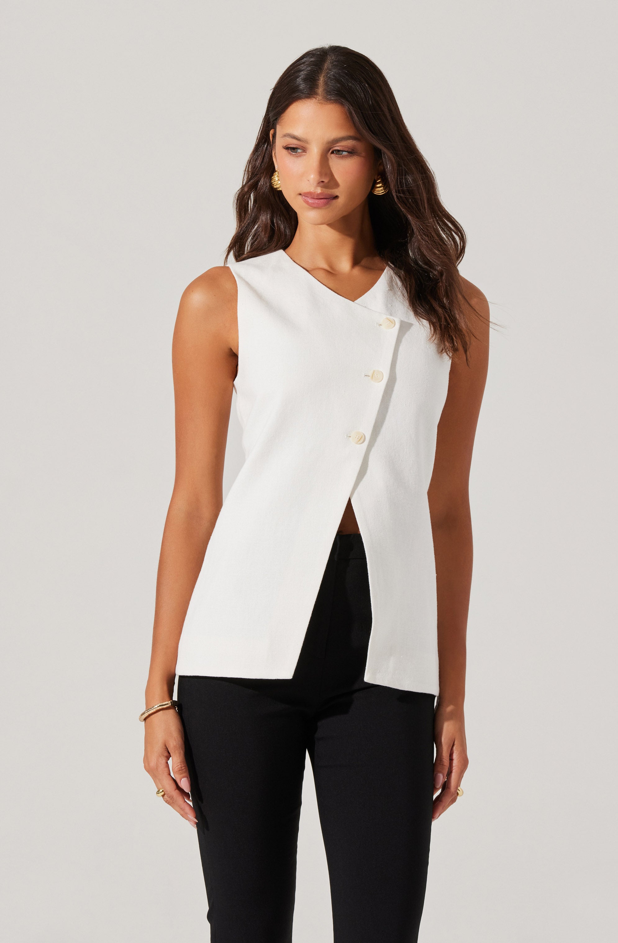 A woman is wearing a sleeveless white vest with a V-neckline and large buttons down the front, paired with black pants.