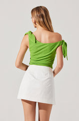 A woman is wearing a bright green, textured, sleeveless top with tied shoulder straps and a loose fit, paired with a high-waisted white mini skirt.