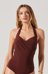 A woman is wearing a sleeveless, halter-neck swimsuit in a deep burgundy color. The swimsuit features gathered and draped fabric detailing at the bust and around the waist, creating a fitted silhouette.