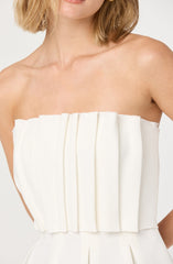 A woman is wearing a strapless white dress with vertical pleats on the bodice. The dress appears to be made of a smooth, structured fabric.