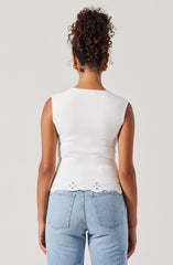 A woman is wearing a sleeveless white top with a scalloped hem and eyelet detailing at the bottom. She is also wearing light blue high-waisted jeans.
