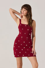 A woman is wearing a sleeveless, fitted red dress with wide straps. The dress features small white floral patterns scattered evenly across the fabric.