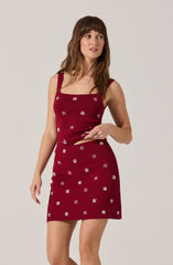 A woman is wearing a matching two-piece outfit consisting of a sleeveless, deep red tank top with wide straps and a fitted, knee-length skirt. Both pieces feature a pattern of small white floral designs.