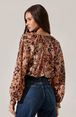 A woman is wearing a long-sleeved blouse with a leopard print pattern in shades of brown, black, and beige. The blouse features a gathered neckline with a small opening at the back, creating a slightly billowed effect on the sleeves and a relaxed fit. She pairs the blouse with high-waisted dark blue jeans.