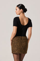 A woman is wearing a fitted black short-sleeve top with a deep scoop back and ribbed texture, paired with a high-waisted leopard print skirt with front pockets.