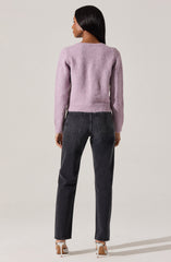 A woman is wearing a soft, fuzzy, light purple sweater with long sleeves and a round neckline, paired with high-waisted, slightly faded black jeans with visible stitching on the back pockets. She is also wearing nude-colored heels with a white ankle strap.
