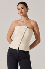 A woman is wearing a strapless, cream-colored, textured top with large, decorative buttons and black high-waisted jeans.