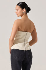 The woman is wearing a strapless, textured, cream-colored top with a zipper at the back and a slightly frayed hem. She has paired it with dark high-waisted jeans.
