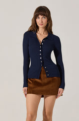 A woman is wearing a long-sleeved, navy blue, ribbed cardigan with a collar and white buttons down the front. She pairs it with a brown corduroy mini skirt.