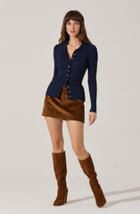 A woman is wearing a fitted, long-sleeved, navy blue button-up cardigan with a collar. She pairs it with a short, brown corduroy skirt and matching brown knee-high boots with high heels.